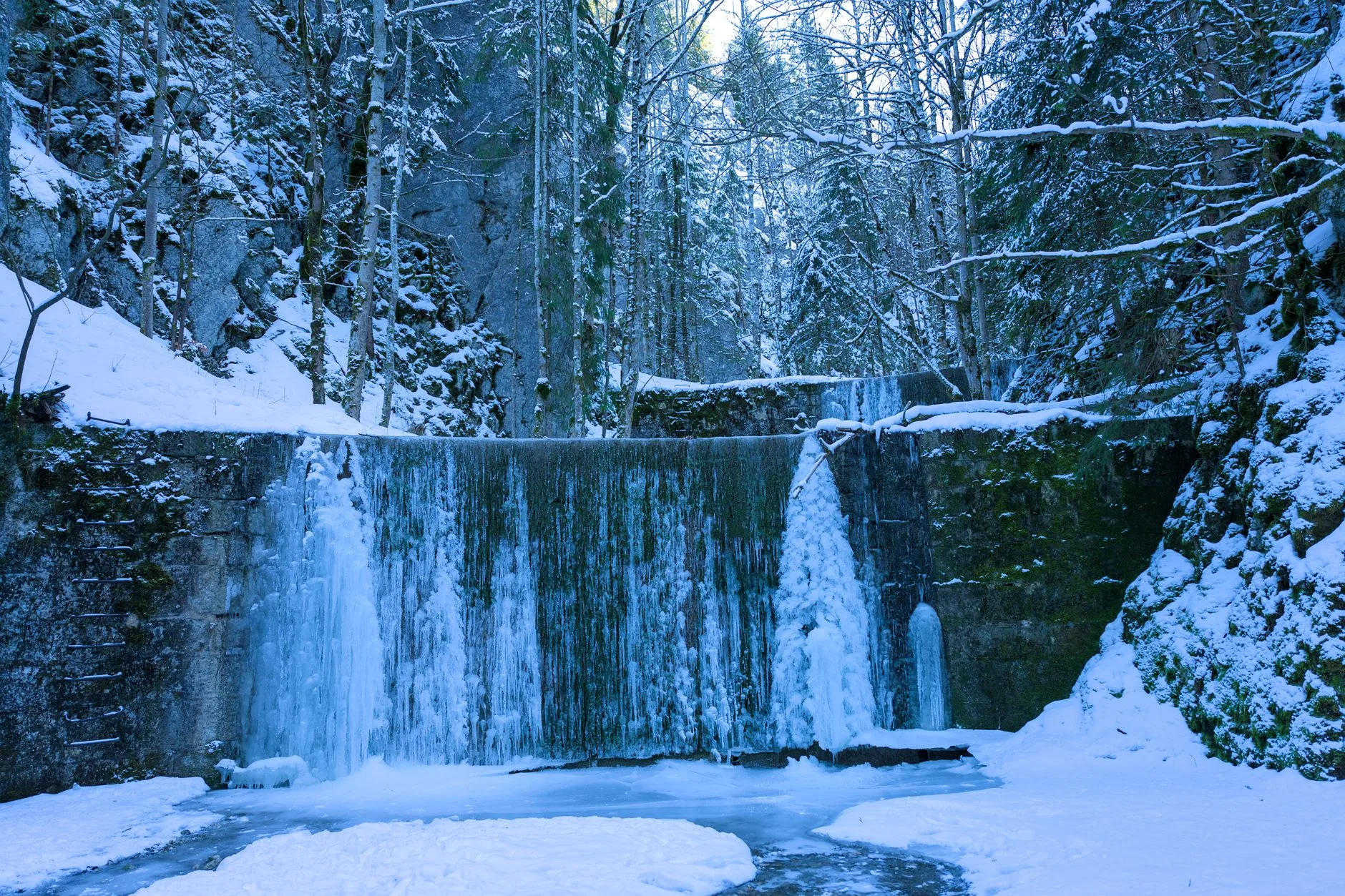 Cascade gelée dans une forêt enneigée du Jura